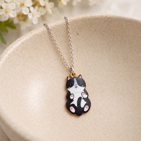 Black and white belly-up cat pendant necklace resting in a speckled ceramic bowl