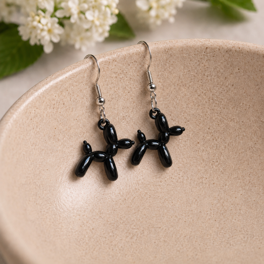 Black Balloon Dog Earrings hanging from a ceramic bowl