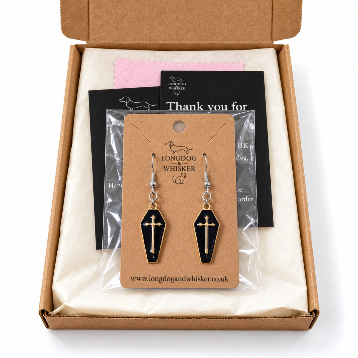 Black and gold-tone coffin cross earrings in Longdog & Whisker postal packaging