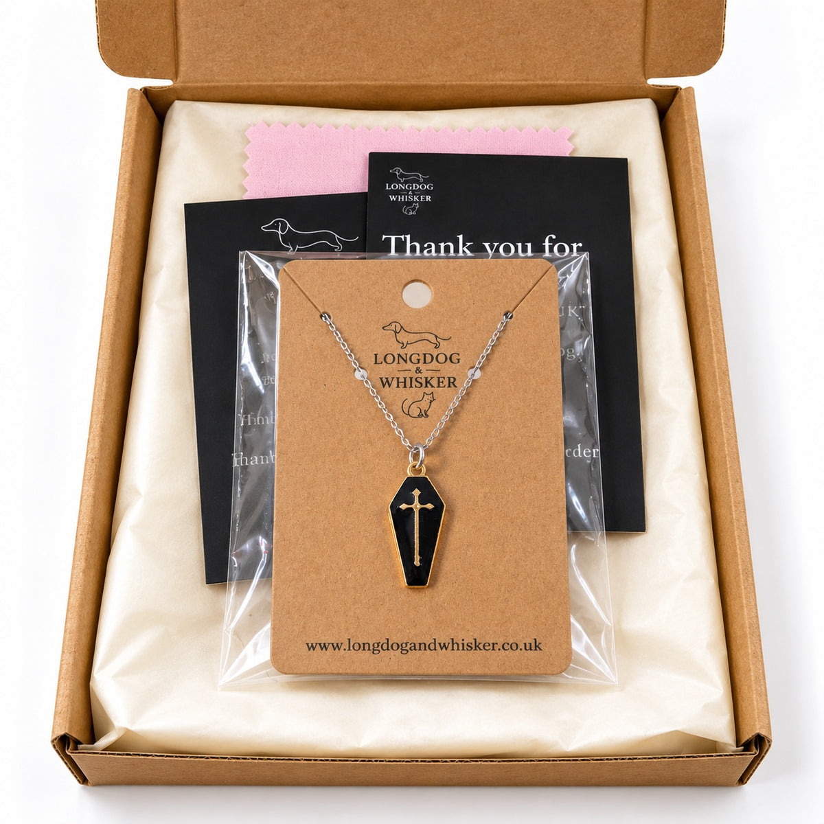 Black and gold-tone coffin cross necklace on a silver-tone chain in Longdog & Whisker postal packaging