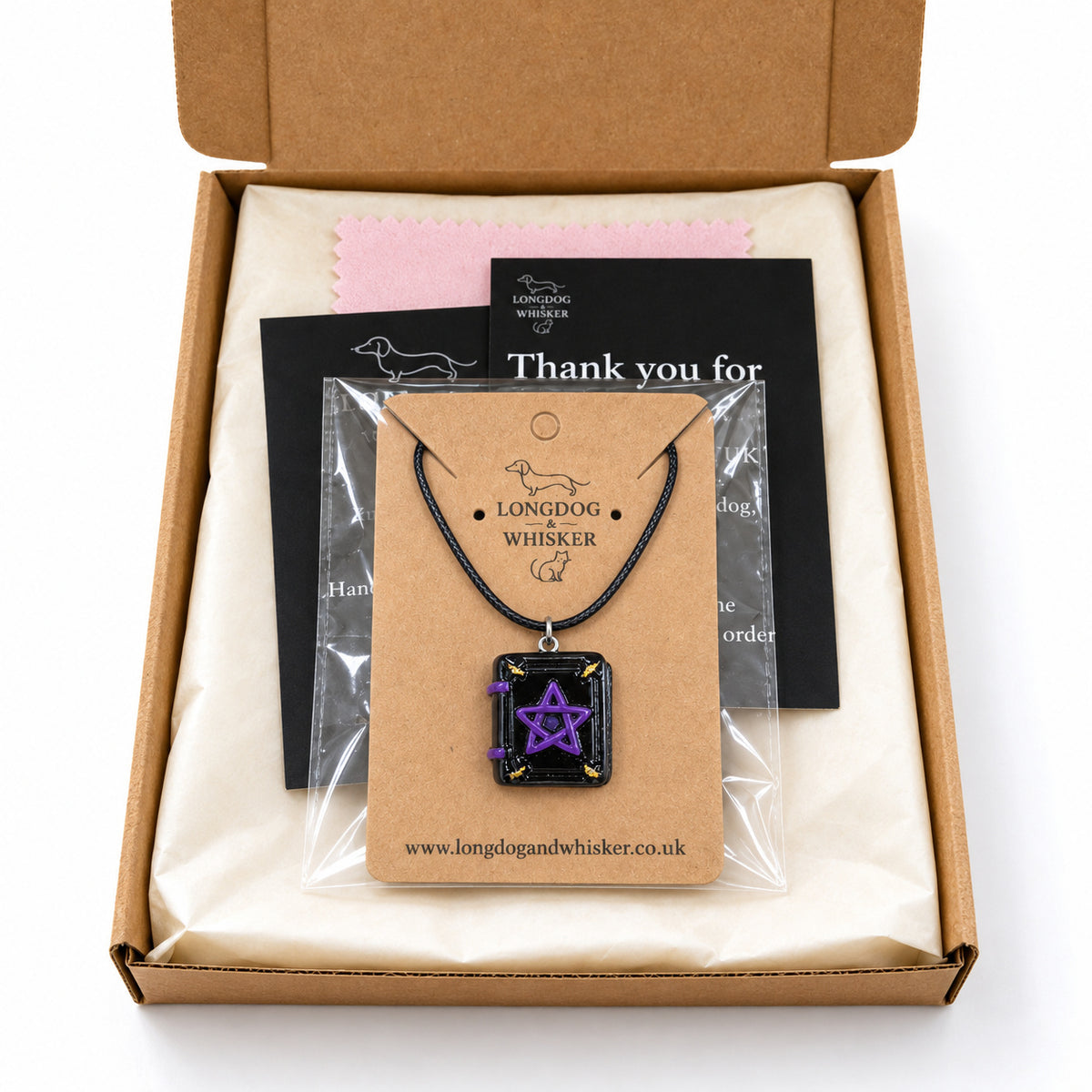 Black cord spellbook necklace on its kraft card in a clear bag inside Longdog & Whisker packaging