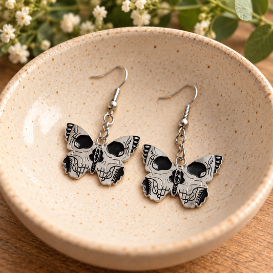 Black and silver skull-wing butterfly drop earrings in a ceramic bowl