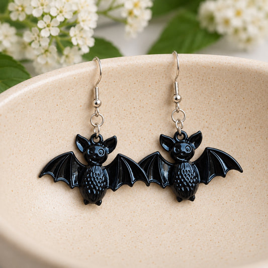 Glossy black smiley bat earrings resting in a cream ceramic bowl