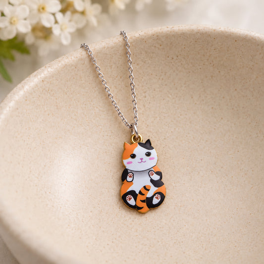 Calico belly-up cat pendant necklace resting in a speckled ceramic bowl