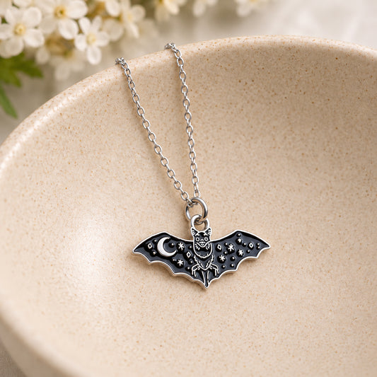 Black celestial bat pendant with moon and star details resting in a speckled ceramic bowl