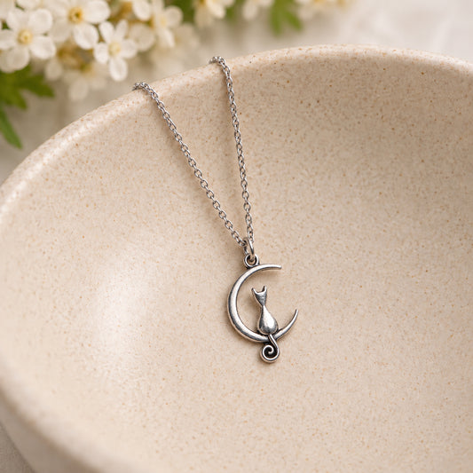 Silver cat and crescent moon necklace resting in a speckled ceramic bowl.