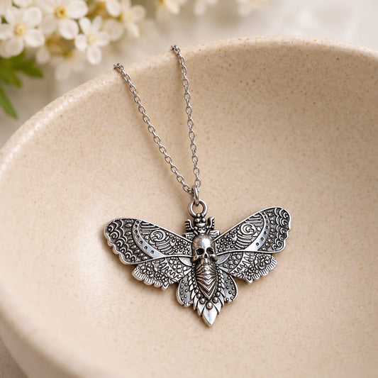 Silver skull moth pendant and silver chain resting in a speckled ceramic bowl