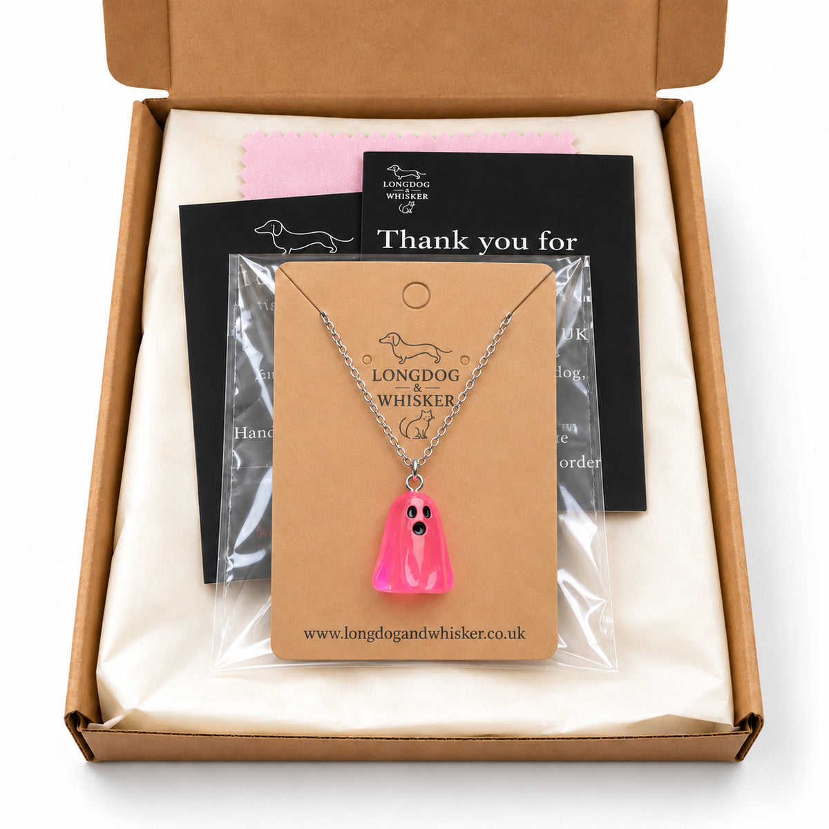 Translucent bright pink ghost necklace on its card in Longdog & Whisker postal packaging.