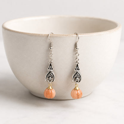Batty Pumpkin Earrings hanging on a ceramic bowl
