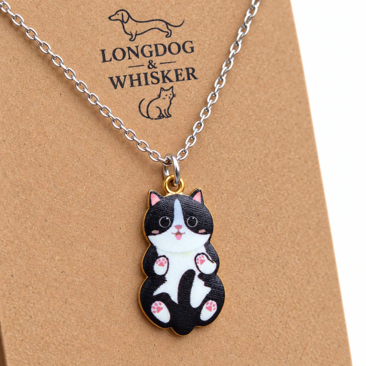 Close-up of the black and white cat pendant with pink paw pads, a tiny tongue and mixed-tone fittings