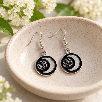Black crescent moon and pentagram earrings resting in a speckled ceramic bowl
