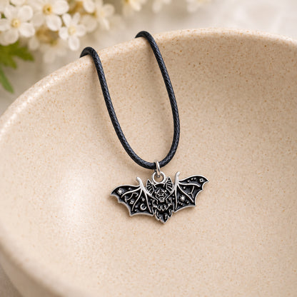 Black fanged bat pendant and black cord resting in a speckled ceramic bowl