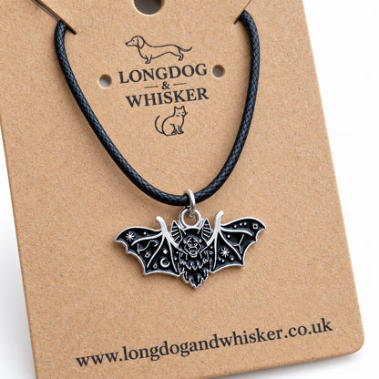 Close-up of the black fanged bat necklace on black cord showing its face and silver-tone wing patterns