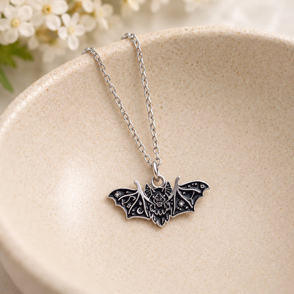 Black fanged bat pendant and silver chain resting in a speckled ceramic bowl