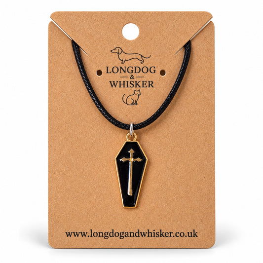 Black coffin necklace with gold-tone cross on black cord, displayed on a Longdog & Whisker kraft card