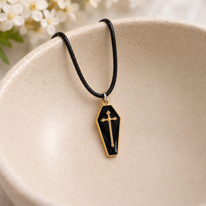 Black and gold-tone coffin cross necklace on black cord resting in a speckled ceramic bowl