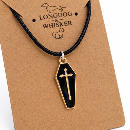 Close-up of the glossy black coffin pendant, gold-tone cross and border, silver-tone connector and black cord