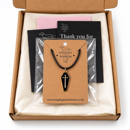 Black and gold-tone coffin cross necklace on black cord in Longdog & Whisker postal packaging