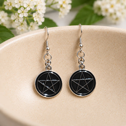 Black pentagram drop earrings resting in a speckled ceramic bowl