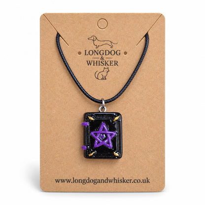 Black and purple spellbook necklace on black cord on a Longdog & Whisker kraft card against white