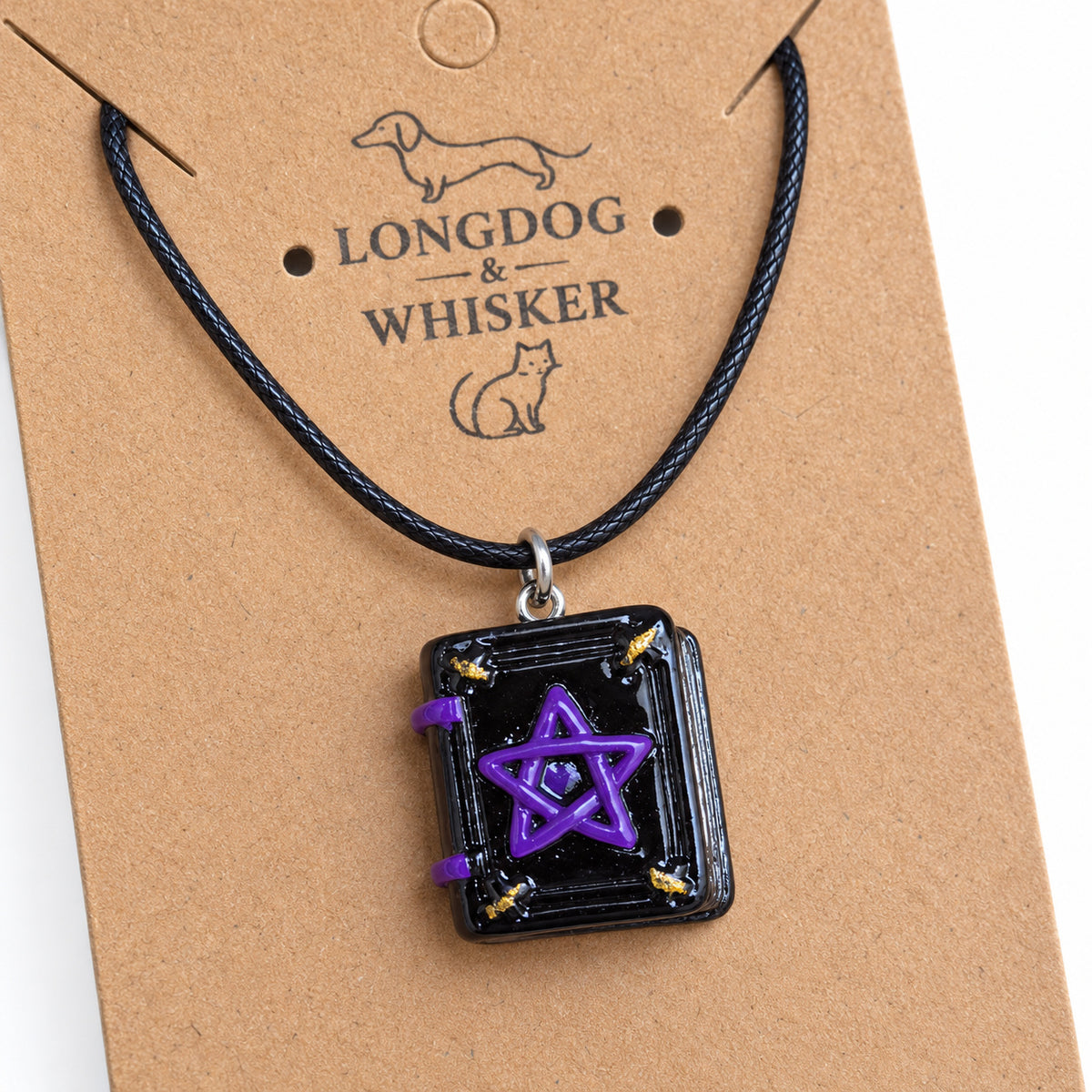 Close-up of the spellbook pendant on black cord showing purple pentagram, gold-coloured corners and page detailing