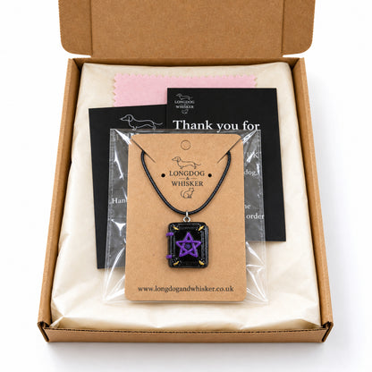 Black cord spellbook necklace on its kraft card in a clear bag inside Longdog & Whisker packaging