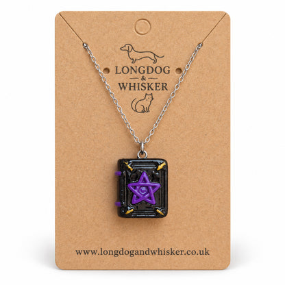 Black and purple spellbook necklace on a silver-tone chain on the Longdog & Whisker kraft card against white
