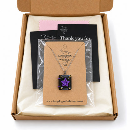 Spellbook necklace on its branded kraft card in a clear bag inside Longdog & Whisker kraft gift packaging