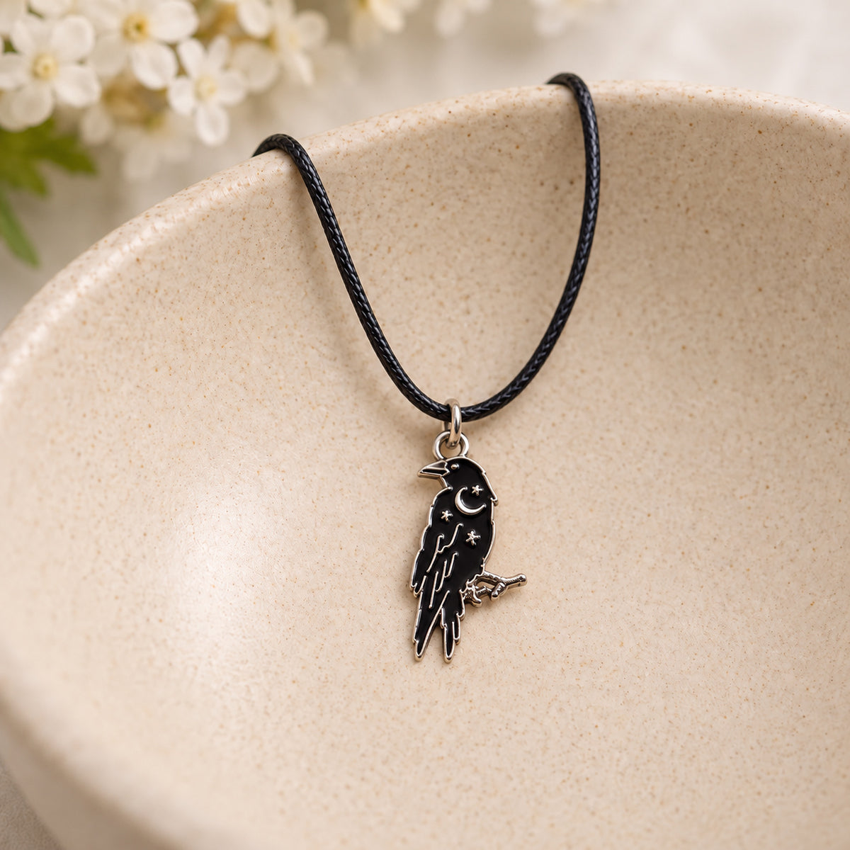 Black raven pendant and black cord resting in a speckled ceramic bowl