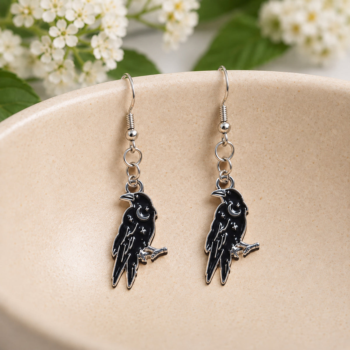 Black Raven Crescent Moon Drop Earrings in a speckled ceramic bowl