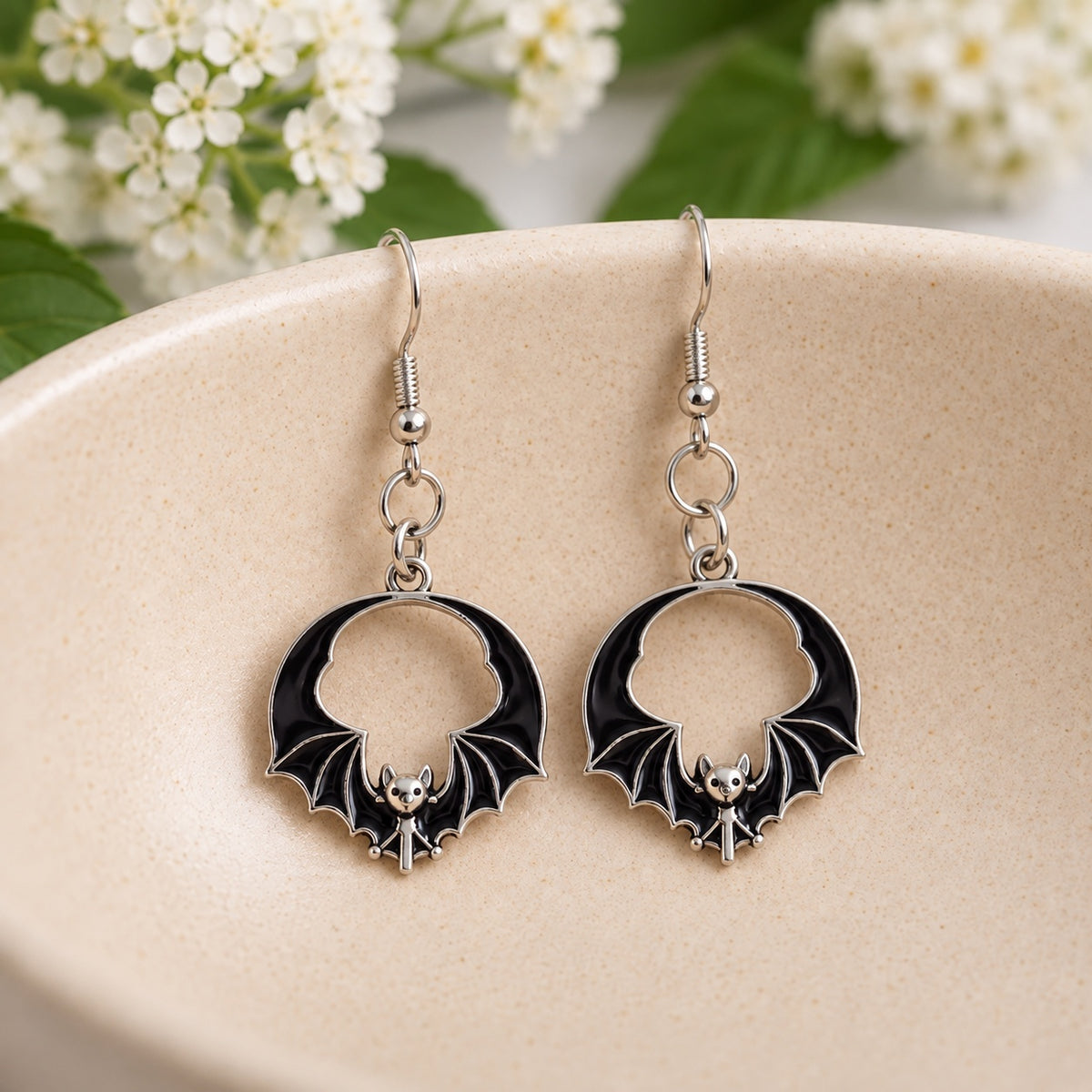 Pair of black round wing bat earrings resting in a cream ceramic bowl