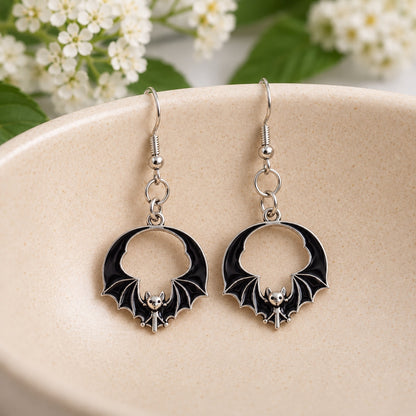 Pair of black round wing bat earrings resting in a cream ceramic bowl