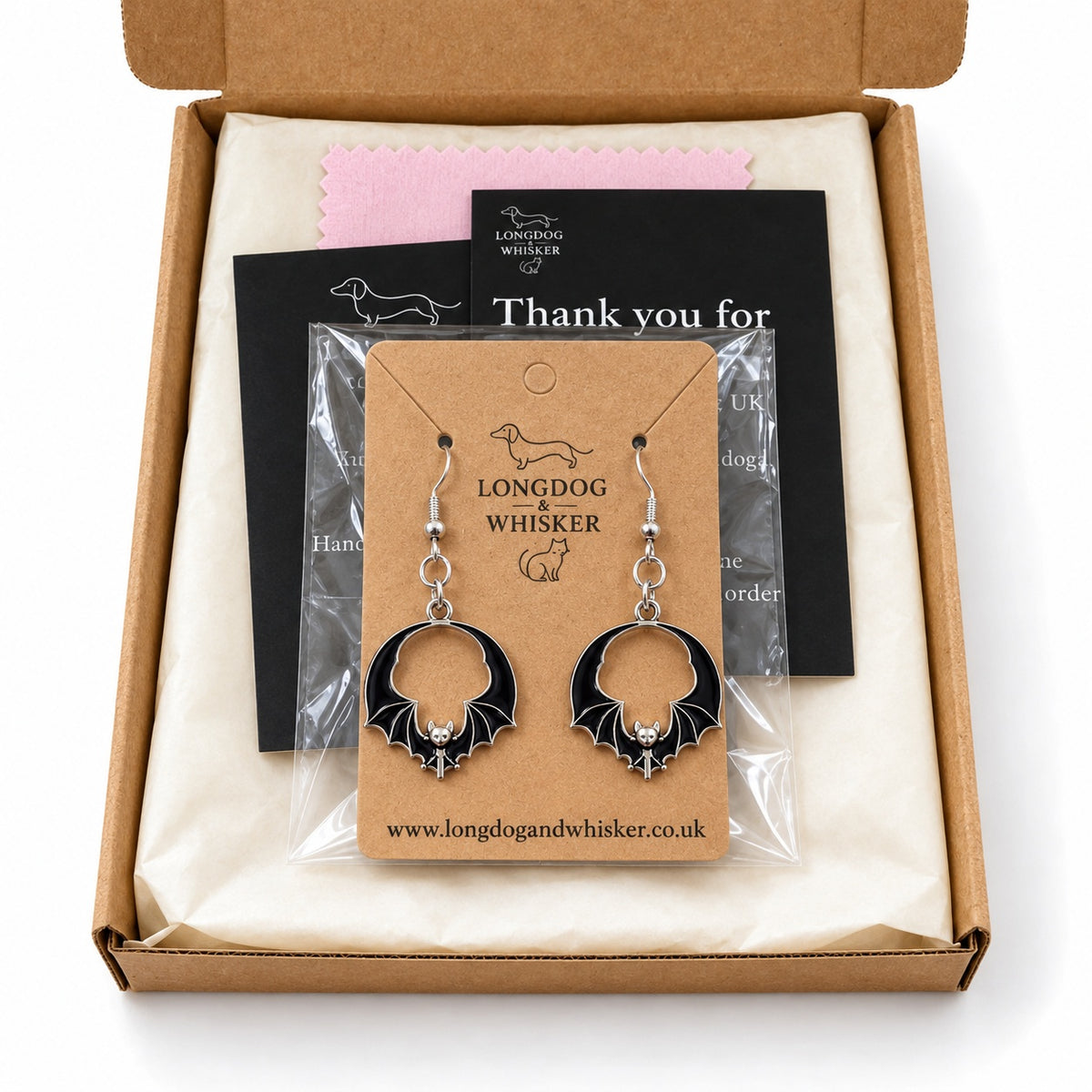 Black round wing bat earrings on their kraft card inside Longdog & Whisker packaging