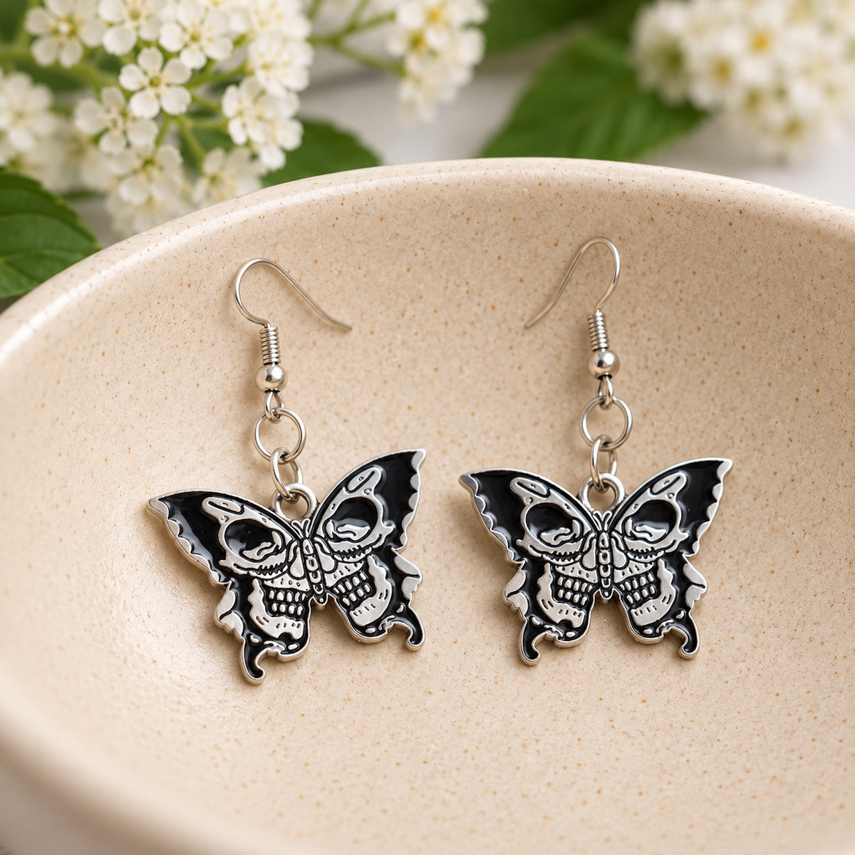 Double skull butterfly earrings in a speckled ceramic bowl