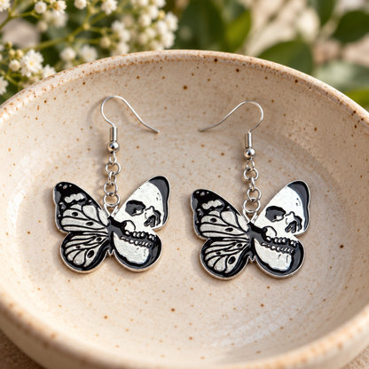 Black and silver skull butterfly drop earrings in a speckled ceramic bowl