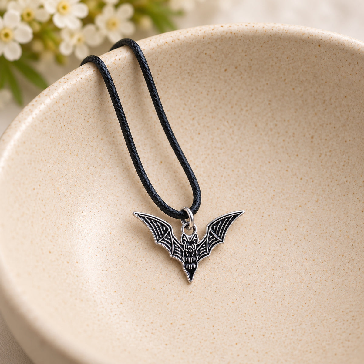 Black skeletal bat pendant and black cord resting in a speckled ceramic bowl