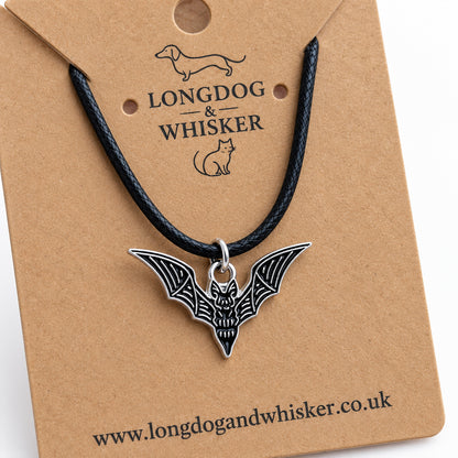 Close-up of the black skeletal bat necklace on black cord, showing its silver-tone bone detailing