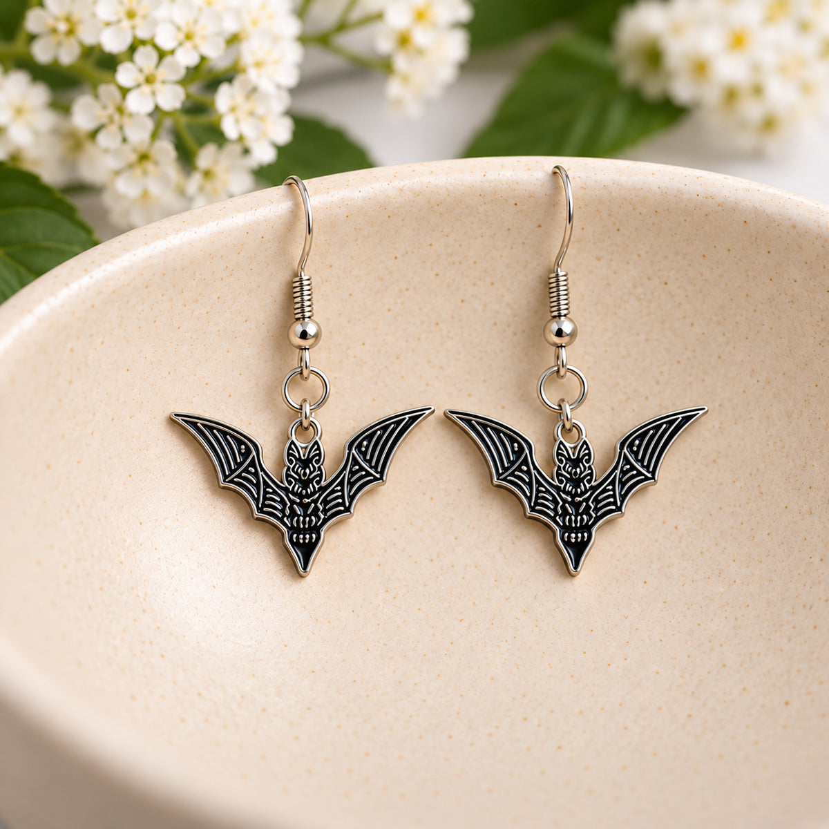 Black skeletal bat earrings displayed in a speckled ceramic bowl