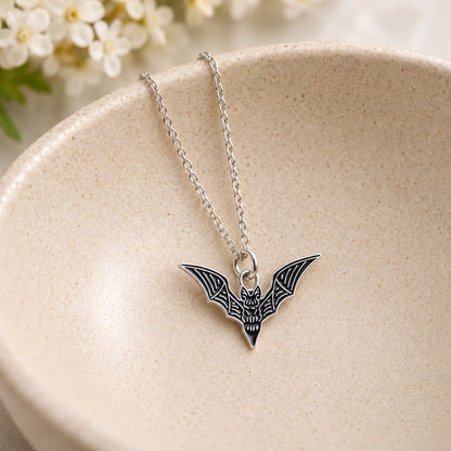 Black skeletal bat pendant and silver chain resting in a speckled ceramic bowl