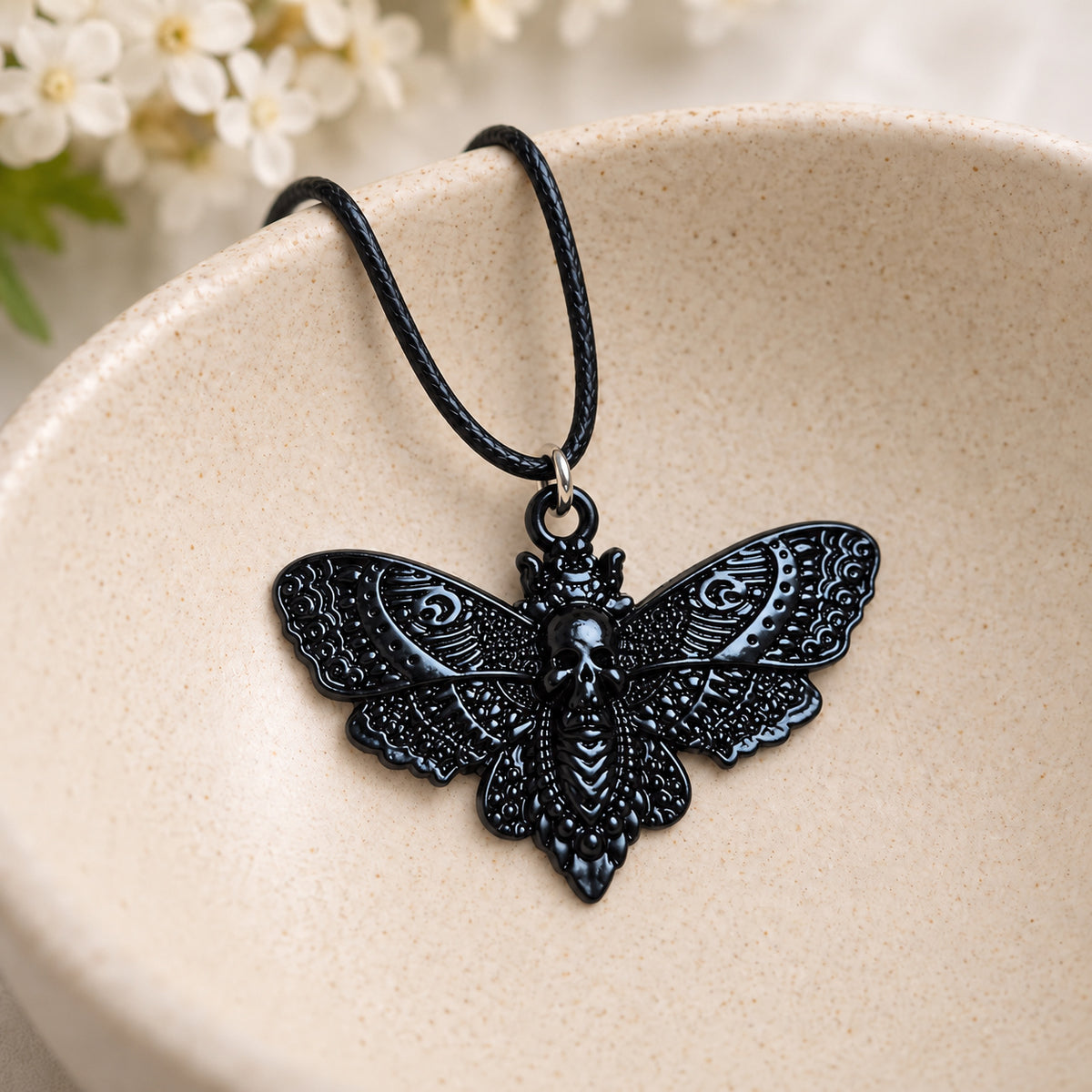 Glossy black skull moth pendant and black cord resting in a speckled ceramic bowl