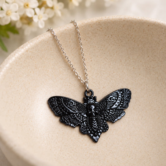 Glossy black skull moth pendant and silver chain resting in a speckled ceramic bowl