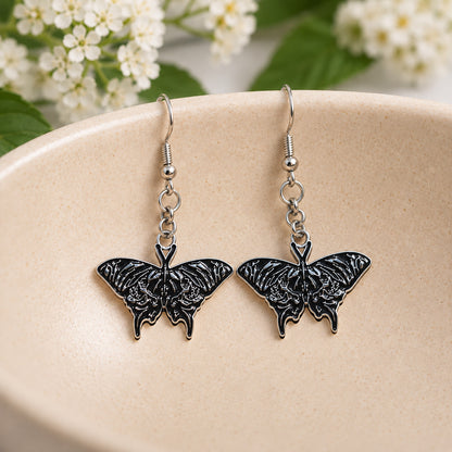 Black skull moth earrings resting in a speckled ceramic bowl