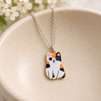 Orange, black and white calico cat pendant on a silver chain in a speckled ceramic bowl