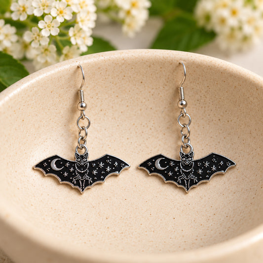 Black celestial bat earrings resting in a speckled ceramic bowl