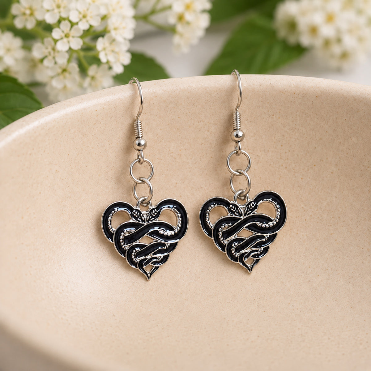 Black and silver-tone entwined snake heart earrings in a ceramic bowl