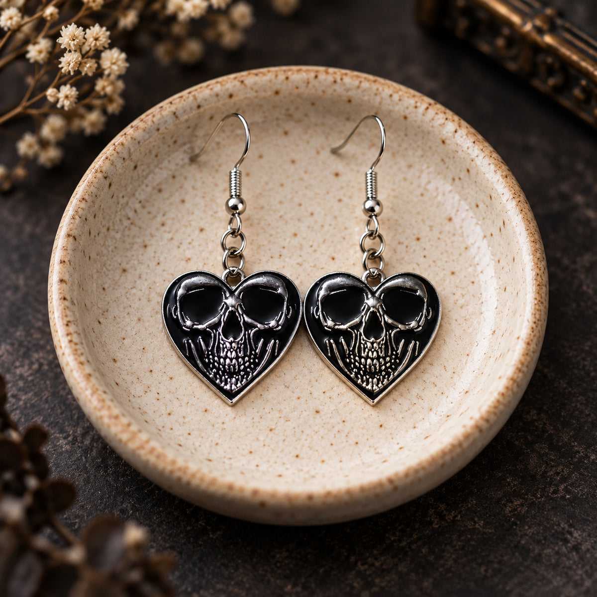 Front-facing skull heart drop earrings in a speckled ceramic jewellery dish