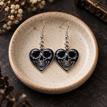 Front-facing skull heart drop earrings in a speckled ceramic jewellery dish
