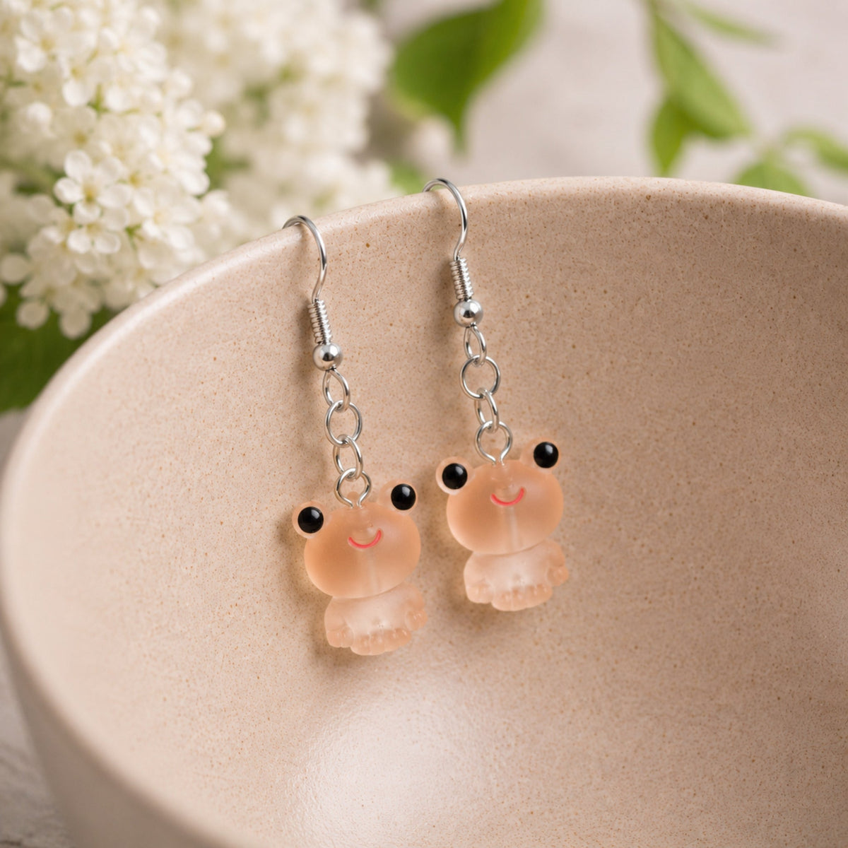 Frosted Frog in Apricot Earrings hooked over a ceramic bowl