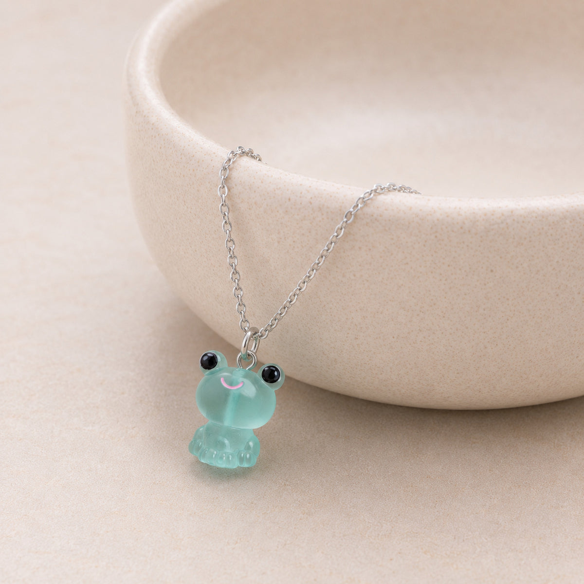 Frosted Frog in Aqua Necklace displayed on a ceramic bowl