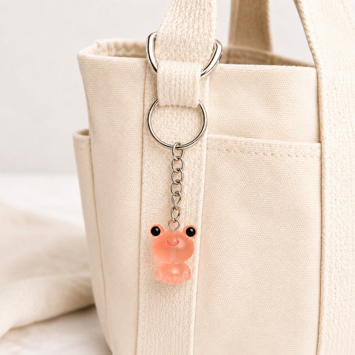 Frosted Frog in Coral Keyring & Bag Charm attached to a cream canvas bag